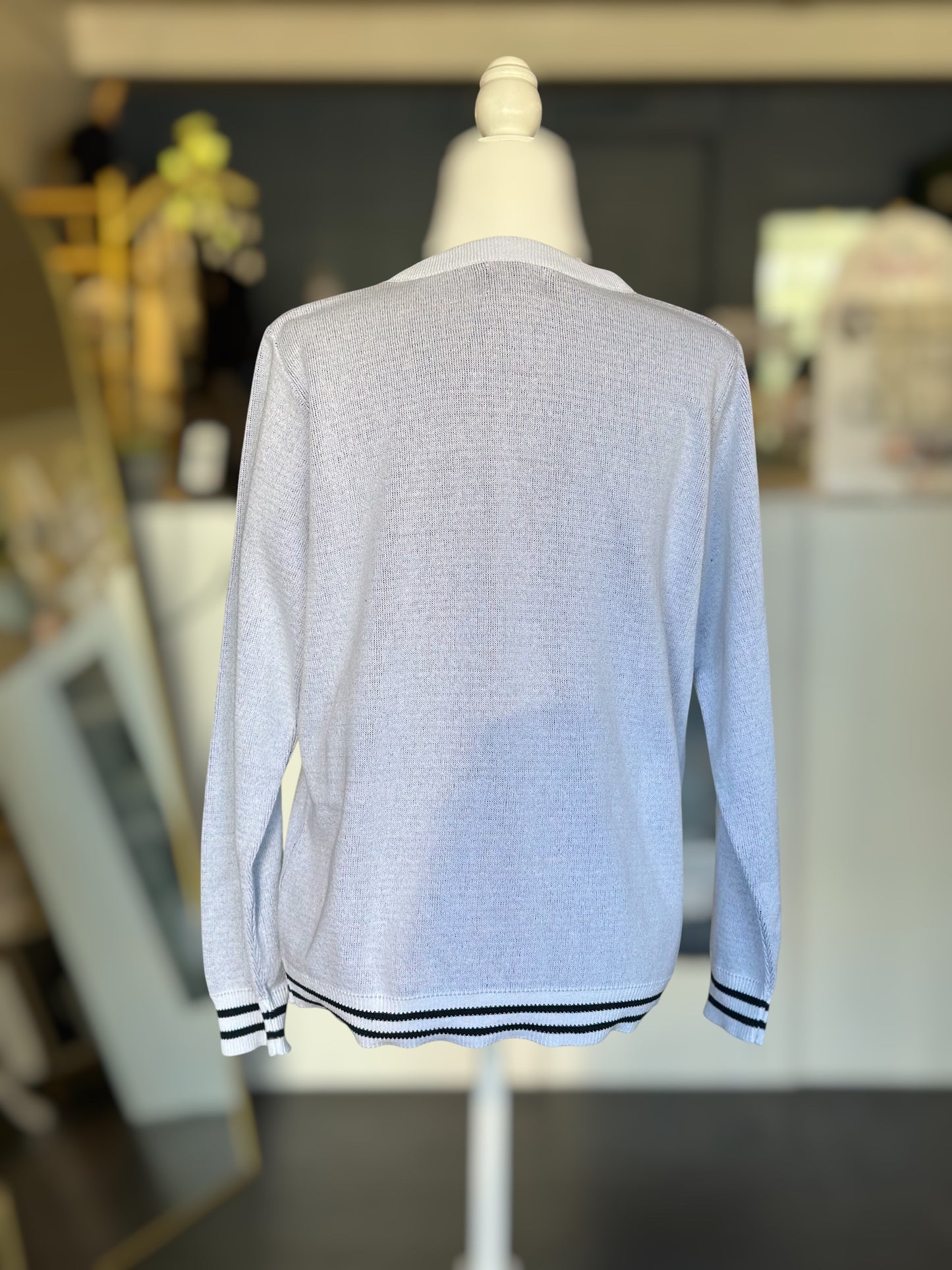 Back view of a lightweight white knit sweater with striped ribbed hem and cuffs, displayed on a mannequin. We Are.