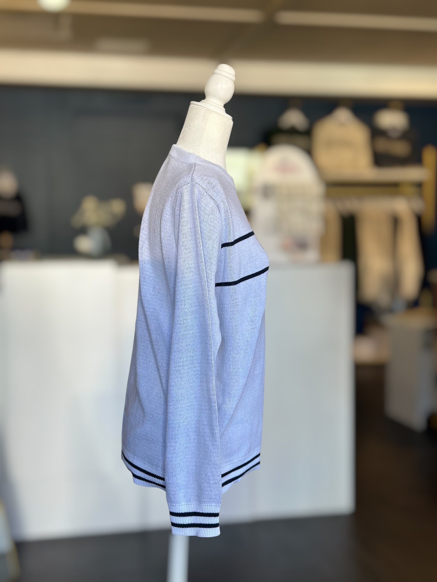 Side profile of a lightweight white knit sweater with black “WE ARE” lettering across the chest, shown on a mannequin.